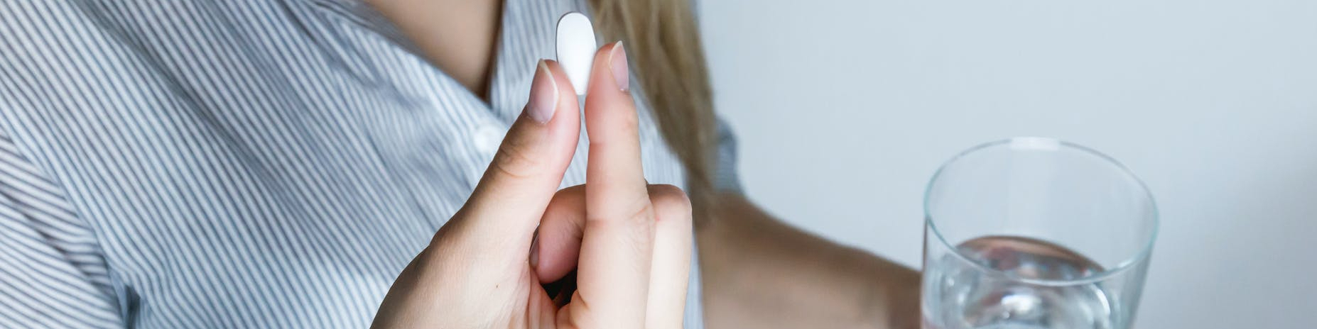 woman holding half full glass and white medicine pill